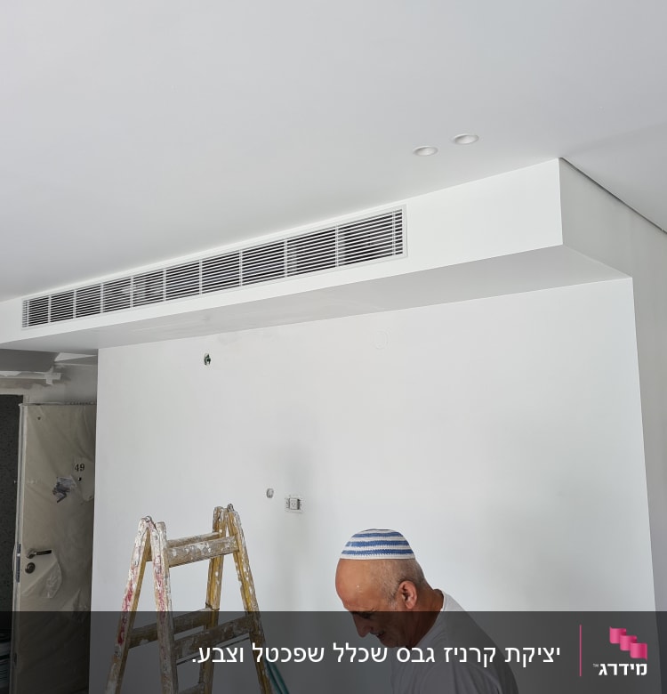 אדם עובד על קיר גבס עם סולם וחומרי בנייה